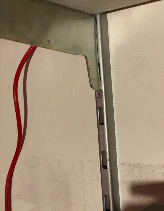Metallkonsol monterad på väggskena med synlig skruv och röd kabel i bakgrunden.