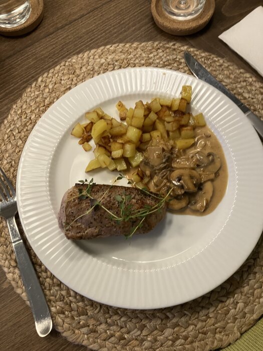 Helstekt fläskfilé med stekt tärnad potatis och svampsås på kastanjechampinjoner, serverat på en vit tallrik.