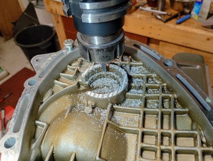 Fräs som bearbetar metalllock på primärhus för att ge plats åt ny komponent, metallspån synliga. Verktygsbord i bakgrunden.