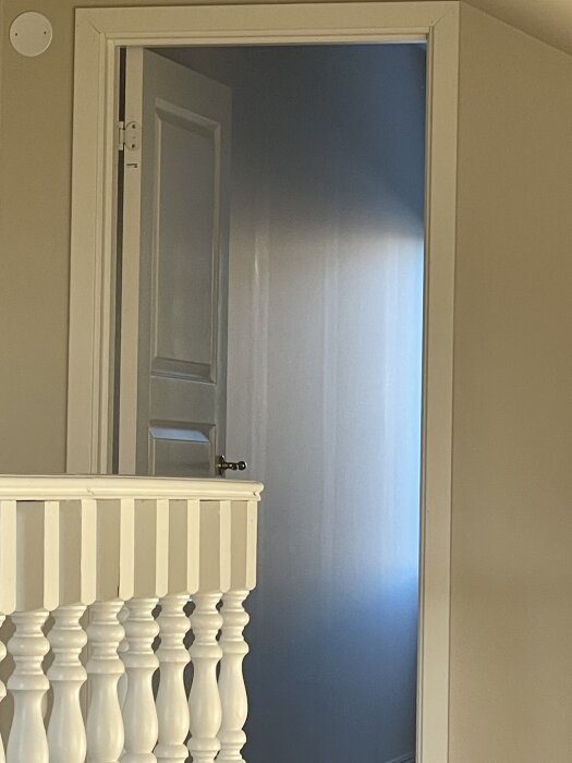 Nyinnervägg med synliga vertikala linjer och skarvar, tagen rakt framifrån, med dörr i bakgrunden och träräcke i förgrunden.