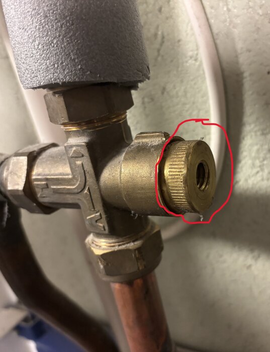 Ventil på fjärrvärmesystem med mässingdel, omgiven av röd markering, visar vred som lossnat och problem med varmvatteninställning.