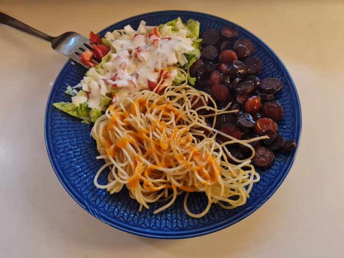 Tallrik med spaghetti med sås, stekta korvbitar och sallad med grönsaker och dressing.