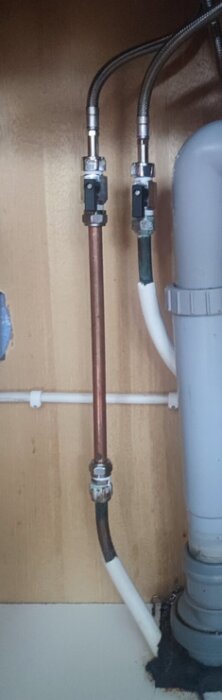 Kopparrör och två flexibla slangar under diskbänken anslutna till VVS-ventiler och ett avloppsrör.