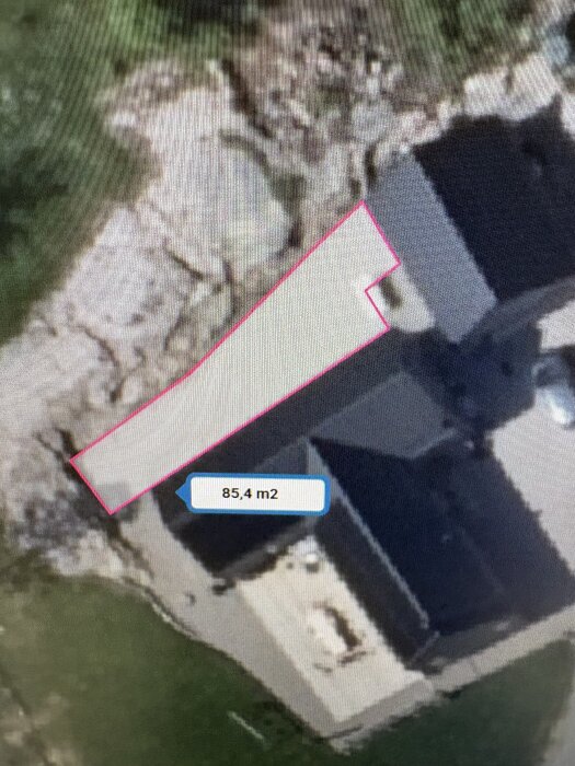 Karta över en bakgård med planerad trall, markerad i rosa, gränsande till ett sluttande berg. Ytan anges som 85,4 kvadratmeter.
