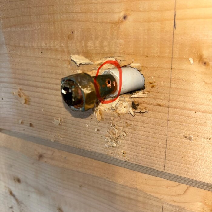 Kopparrör med skada bakom en träpanel, markerat med röd cirkel.
