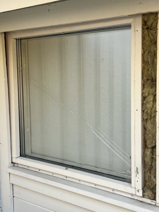 Sprucket glas i ett fönster med vit träram, med delar av glaset ersatta efter inbrottsförsök.