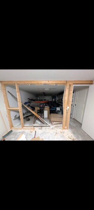 Öppnad garagevägg med borttagna reglar, visar rörig interiör med verktyg och utrustning, inklusive båt med motor och hyllor i bakgrunden.