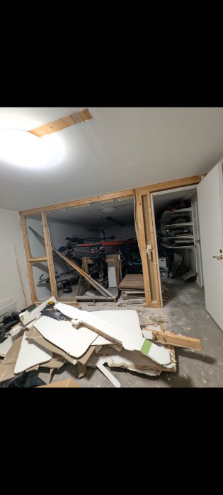 Riven garagevägg med träreglar synliga, gipsskivor på golvet och utrustning i bakgrunden. Öppnad konstruktion för byggprojekt.