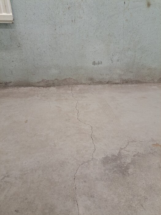 Betongvägg och golv i garage med sprickor och färg som flagnar, visar konditionsproblem inför ombyggnad till hemmagym.