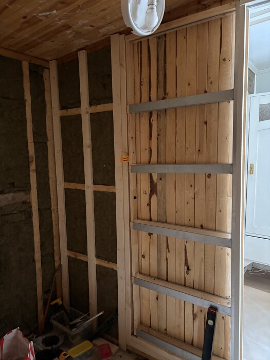 Skjutdörrsram byggd av träpaneler i ett badrum under renovering, med isolering och träreglar på väggen.