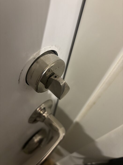 Dörrhandtag och delvis borttagen låscylinder på en dörr, personen behöver hjälp att ta bort låset för att byta låscylindern.