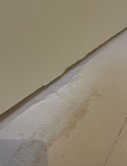 Vägg med ojämna spackellinjer och slipdamm, som visar brist på jämn slipning vid renovering.