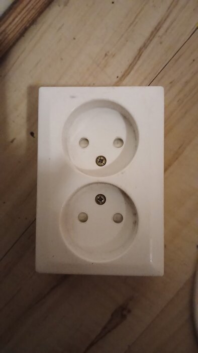 Vit dubbel vägguttag på en trävägg.