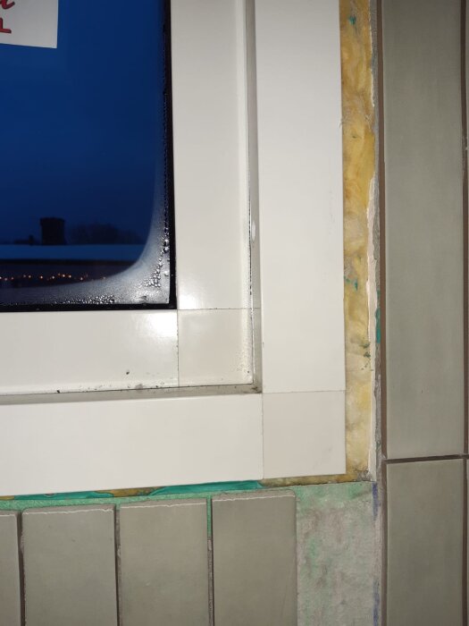Bilden visar ett fönster i ett badrum under renovering. Tätskiktet är synligt med skarvar, samt isolering och kakel som slutar intill fönstret.