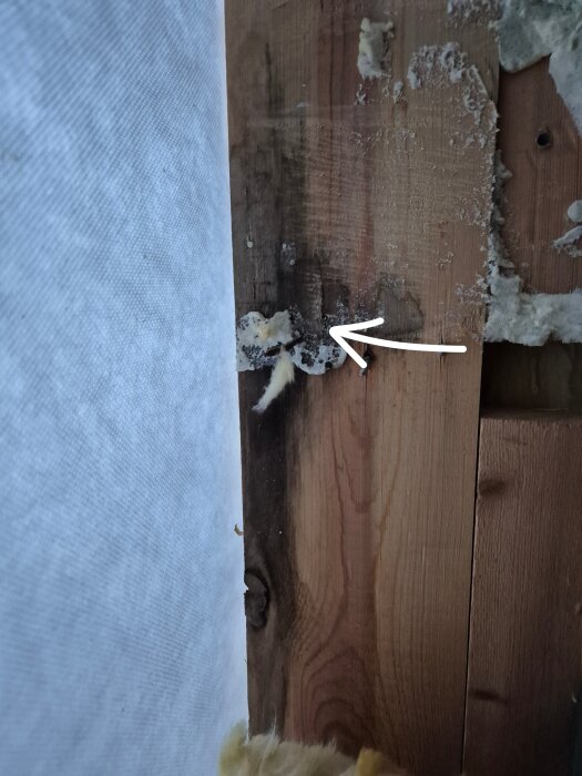 Trävägg med fogskum där ett fönster tagits bort, pil markerar var blecket suttit. Vindpapp synlig till vänster.