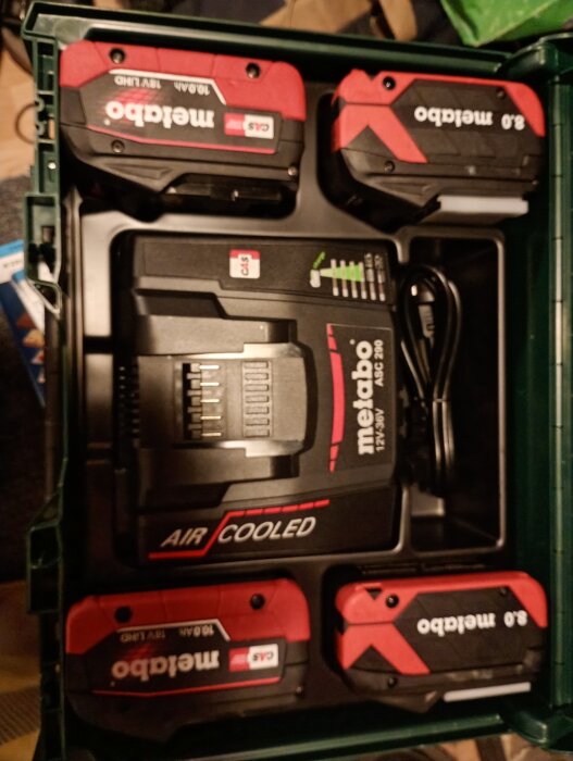 Fyra Metabo-batterier och en batteriladdare i en väska för en kompressor.