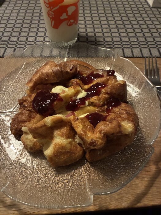 Fläskpannkaka med smör och lingonsylt på en tallrik, serverad med ett glas mjölk bredvid på ett dukat bord.