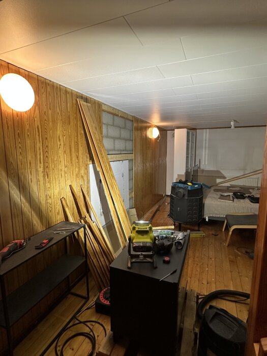 Renovering av gillestuga med rivna paneler, verktyg på bord, och påbörjad demontering av kamin; trägolv och utanpåliggande vägg är synliga.