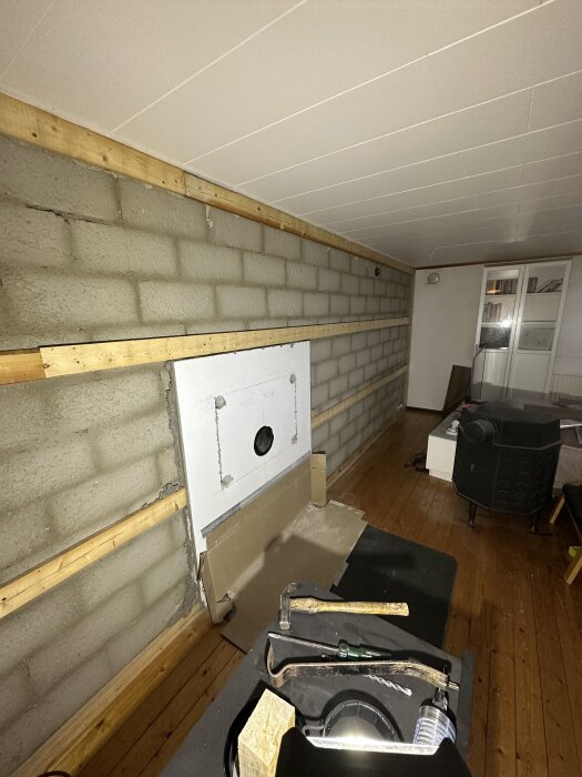 Renoverad källare med exponerad tegelvägg, verktyg såsom hammare och kofot synliga, förberett för ny kamininstallation.
