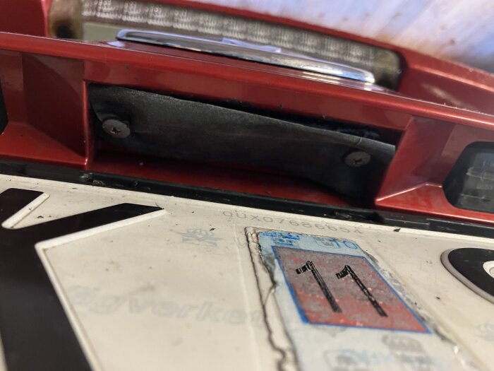 Bilens registreringsskylt i närbild med en röd avgasrörsdetalj ovanför, inklusive en dekal med numret 11.