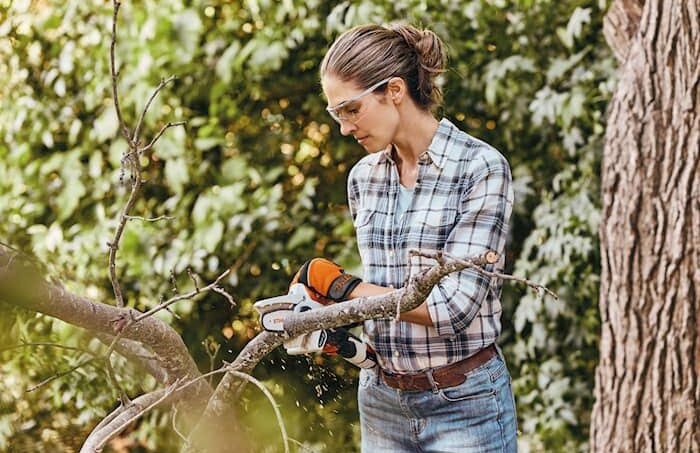 En person använder en STIHL GTA 26 grensåg för att beskära en trädgren i en grön trädgård.