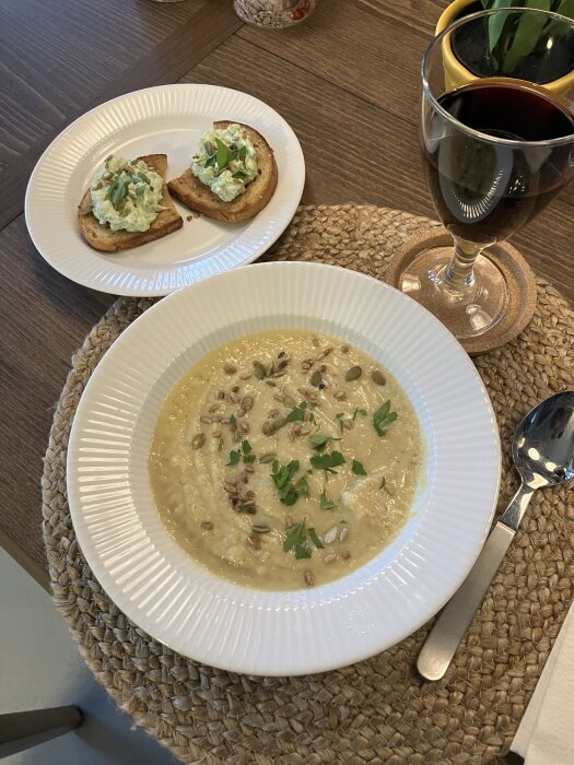 Skål med blomkålssoppa toppad med pumpakärnor och persilja, bredvid bruschetta med mosad broccoli och ett glas rödvin.