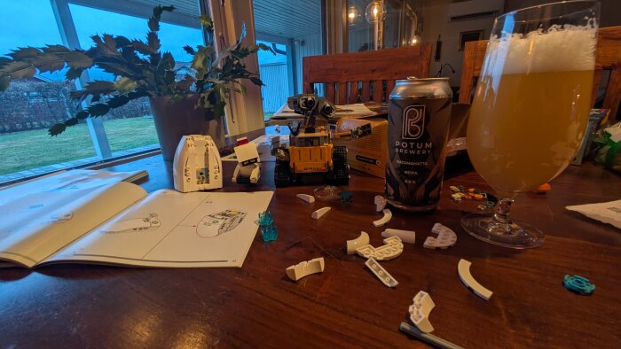 LEGO Wall-E bygge på bord med öl från Potum Brewery, omgiven av byggdelar och instruktioner, i ett hem med utsikt över trädgård.
