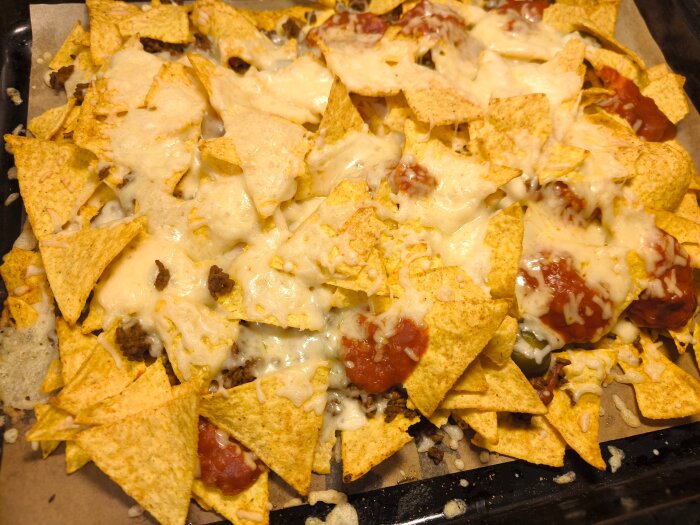 Gratinerade nachos toppade med tacofärs, jalapenos, tacosås och smält ost på en plåt.