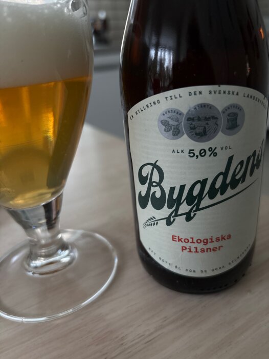 Ekologisk pilsner från Bygdens med en ölglas fylld med blekgul öl och skum.