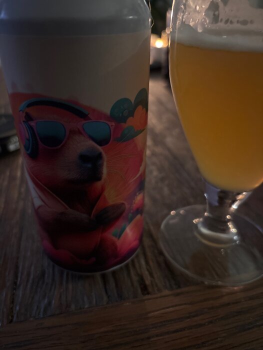 En ölburk med illustration av ett djur i solglasögon och hörlurar bredvid ett glas med blek pilsner på ett bord.