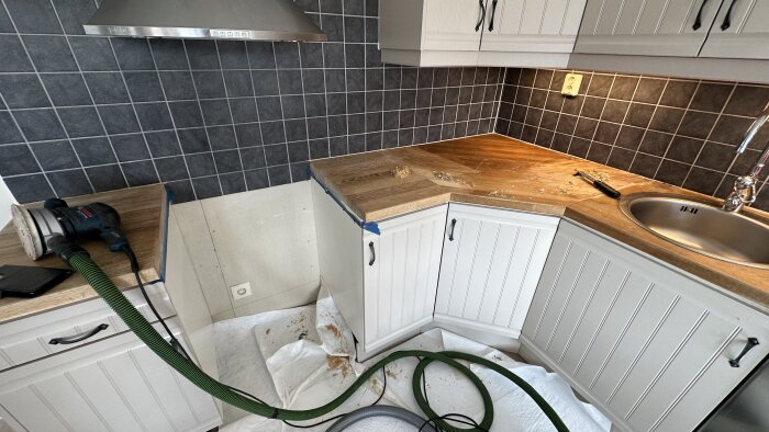Renovering av kök med slipad bänkskiva. Verktyg och slipmaskin syns på vit duk. Grått kakel på väggar.