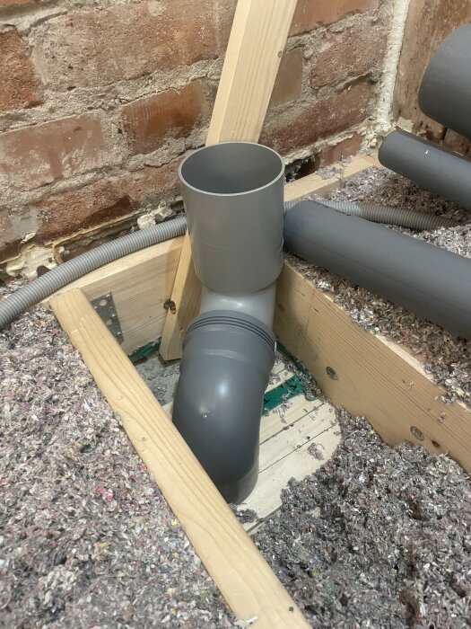 Avloppsrör med stående 90° WC-anslutning och 90°-böj i renoverat badrum, omslutet av träbjälkar och murvägg.
