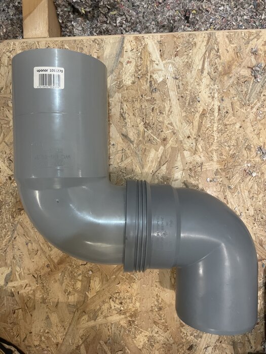Stående 90° grå PVC-rörböj med anslutning på spånskiva, del av avloppssystem för badrumsrenovering.
