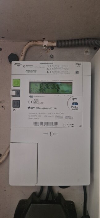 Elcentral med display och knappar, märkt med "Landis+Gyr" och "E360 LTE", kopplad till ett bostadshus med E.ON-nätanslutning.