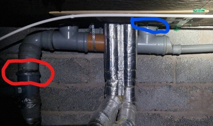 Rörinstallation med rör kopplade i en murad vägg, markerade med röda och blåa cirklar, vilket indikerar potentiella skarvar eller problemområden.