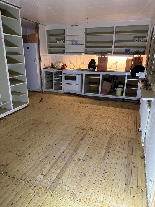 Kök under renovering med öppna hyllor, synliga vitvaror och tomma skåp i ett Myresjöhus från 1969. Golvet är av trä med slitage.