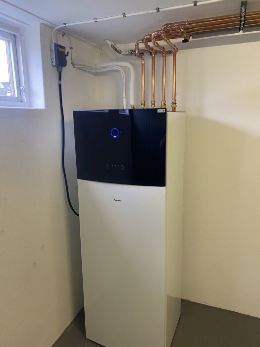 Värmepump luft/vatten-system installerat i vitmålad källare, med kopparrör och elanslutning, del av renoveringsprojekt i Myresjöhus.