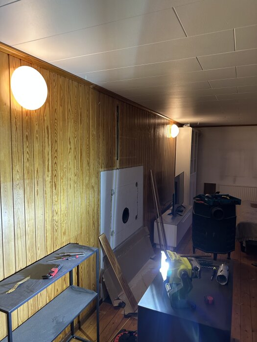 Renovering av gillestuga med omgjord väggpanel, infälld kamin och verktyg på bord i förgrunden.
