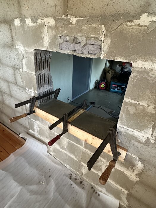 Öppning i murad vägg för ny kamininstallation, omgiven av klämmor och arbetsverktyg, i renoverad gillestuga.