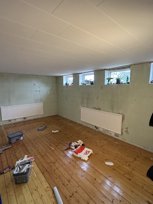 Renovering av gillestuga med nylagd träparkett, vita takplattor, putsade väggar och material utspritt på golvet.