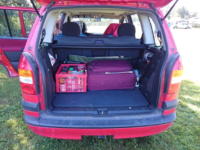 Baklucka på en röd bil fylld med resväska och klappbox med olika saker, som visar hur bilen packats för resa.