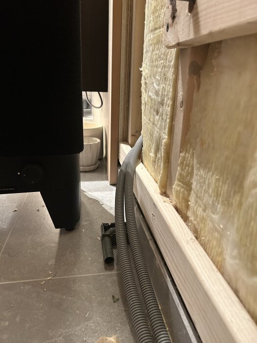 Aggregat på ben nära isolerad vägg med två flexrör som ligger längs golvet.