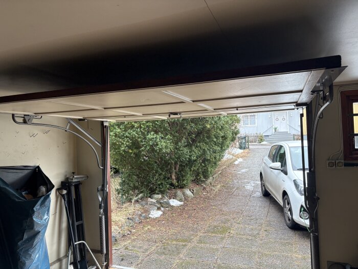 Öppnad garageport sedd från insidan, med vipmekanism och en vit bil parkerad utanför.