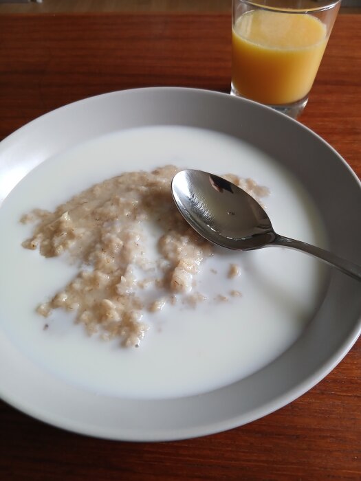Tallrik med havregrynsgröt och mjölk samt ett glas apelsinjuice på träbord.
