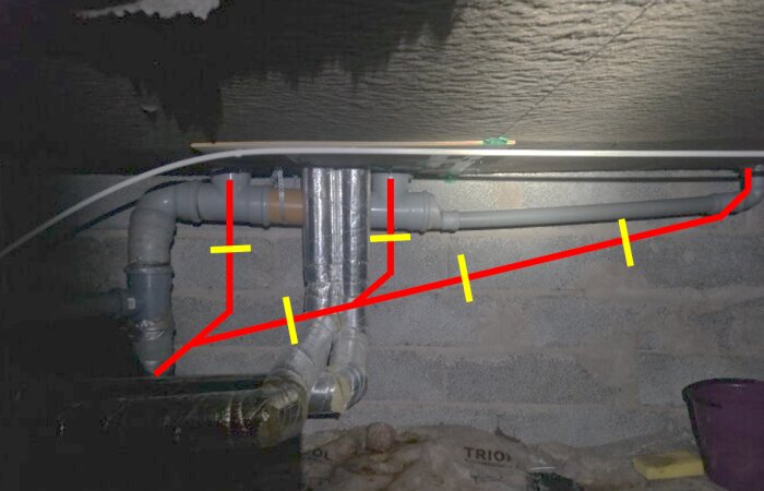 Installation av 110 mm avloppsrör fästa längs grundens vägg med gula markeringar och röda linjer som indikerar rördragning.