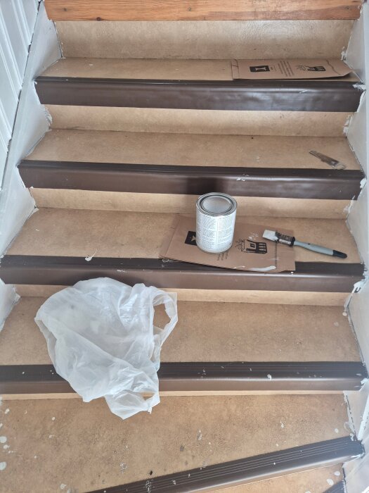 Trappa under renovering med brunt färgade steg; färgburk och pensel synliga.