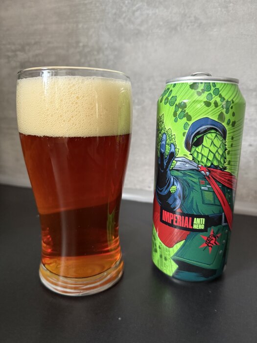 Ett glas överskummande öl bredvid en grönt illustrerad ölburk med texten "Imperial Anti Hero".