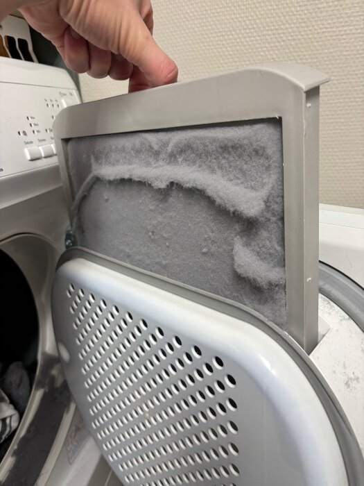 En person tar ut ett torktumlarfilter fullt med ludd från en Electrolux torktumlare, vilket visar överflöd av ludd efter tvättning.