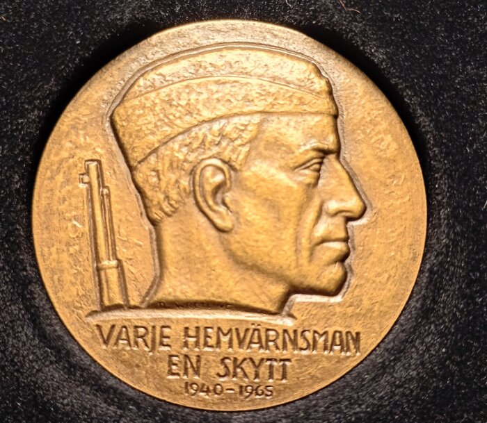 Bronsmedalj med profil av en man i hjälm och gevär; texten "VARJE HEMVÄRNSMAN EN SKYTT 1940-1965" ingraverad.