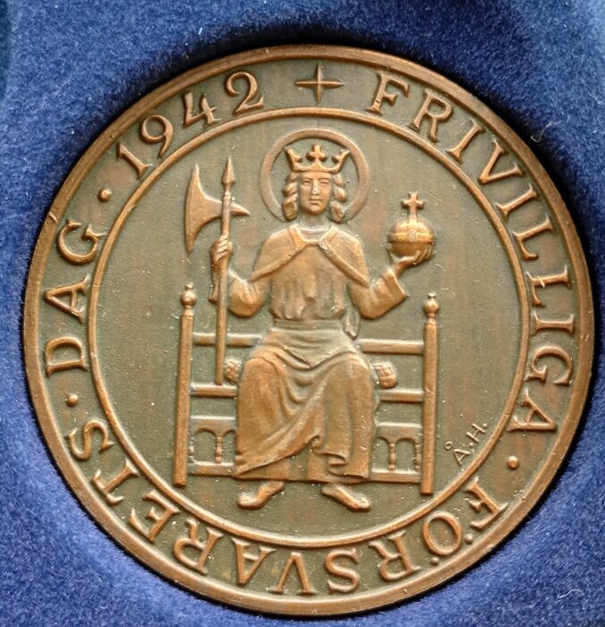 Medalj från 1942, Frivilliga försvarsdag, med kunglig figur som håller en yxa och glob.